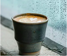 A coffee cup with a heart design placed beside a rainy window