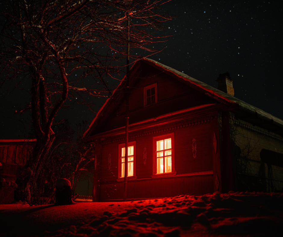 The Family flash fiction cover photo: a house with internal orange lighting, a bare tree, and the dark sky above.