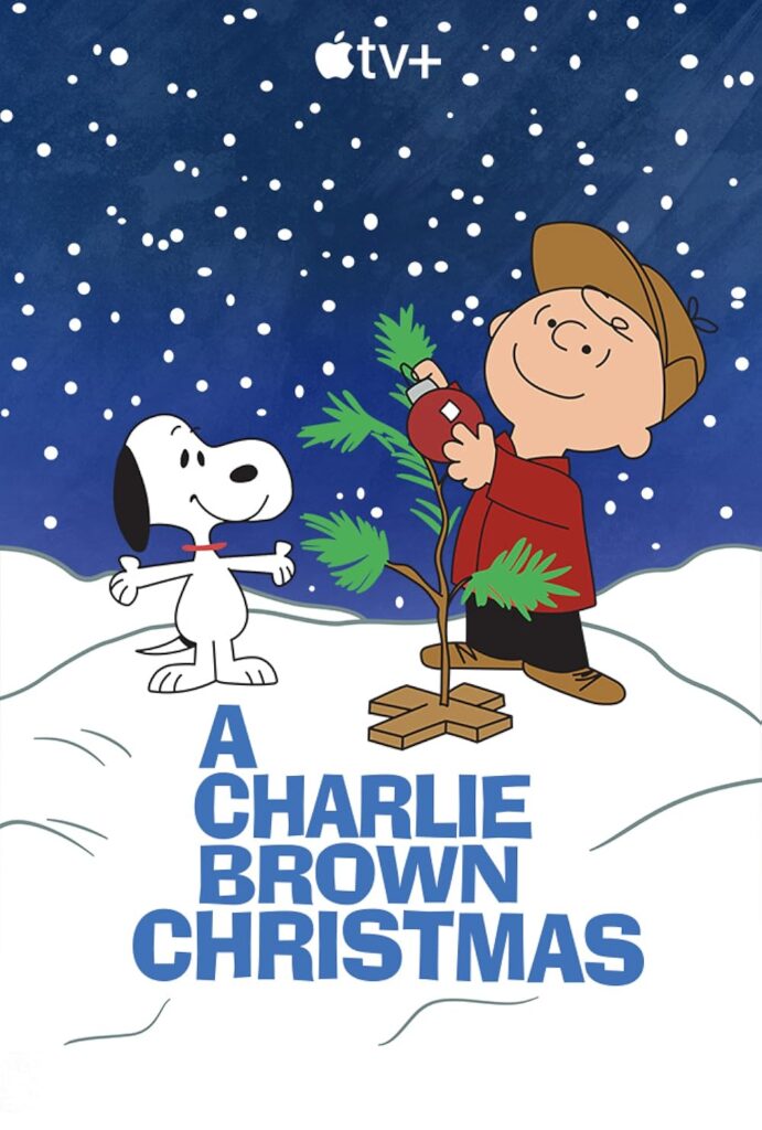 Charlie brown stands beside his tree with Snoopy, holding a red ornament while snow falls.